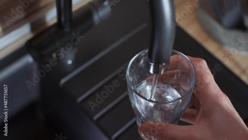 Close-up of a man's hand pouring filtered water into a glass from a kitchen faucet. Clean, healthy lifestyle concept.  