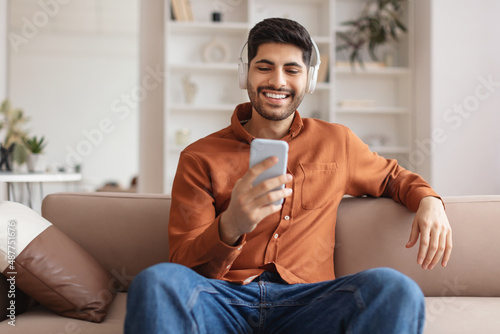 Photo Smiling bearded man in wireless headhones using cellphone
