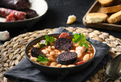 Fabada with chorizo, morcilla, sausage, haricot on black background. Spanish traditional warming dinner. Close up.