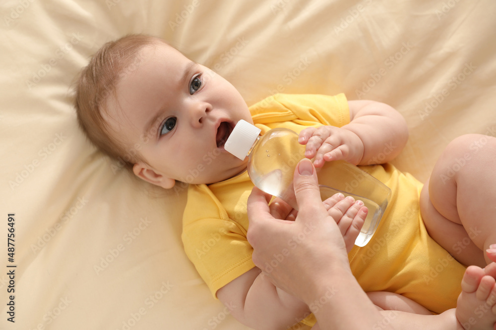 Mother and baby with bottle of massage oil on bed, top view Mother and baby with bottle of massage oil on bed, top view