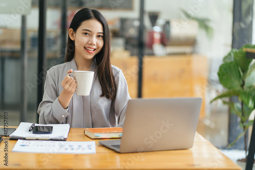 Portrait of young businesswoman sitting in office in front of computer and taking notes in notebook.Girl writer works on book,journalist writes article.Freelancer works remotely.