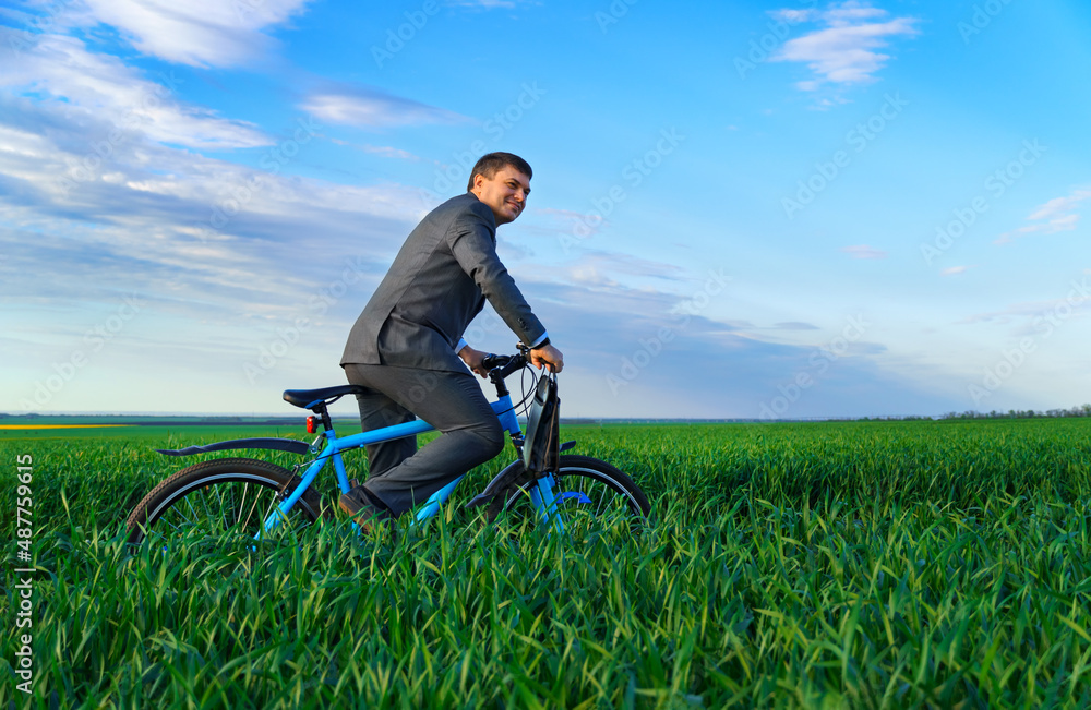 businessman rides a bicycle through a green grass field, dressed in a business suit, he has a briefcase and documents, beautiful nature in spring, business concept businessman rides a bicycle through a green grass field, dressed in a business suit, he has a briefcase and documents, beautiful nature in spring, business concept
