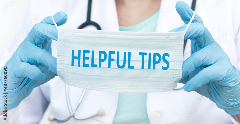HELPFUL TIPS text on protective blue face mask in the hands of a doctor, medical concept HELPFUL TIPS text on protective blue face mask in the hands of a doctor, medical concept