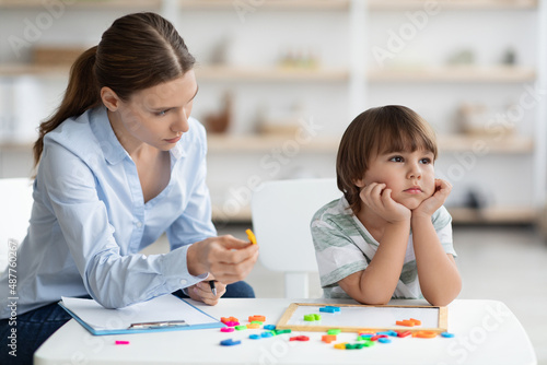 Bored sad little boy refusing to cooperate with teacher, ignoring speech therapist with letters at office, free space photo