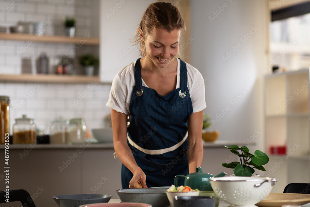 Young woman setting a table for lunch. Smiling happy woman preparing a delicious food. Young woman setting a table for lunch. Smiling happy woman preparing a delicious food.