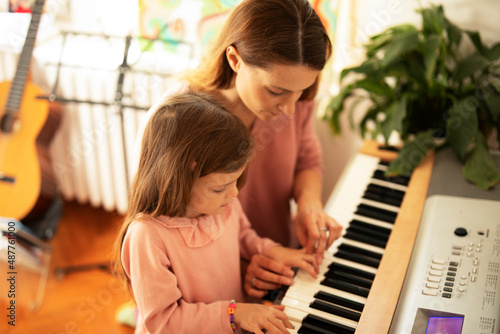 Woman and girl playing a piano. Beautiful mom teaching her daughter playing a piano...