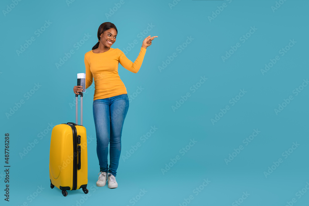 Travel Offer Concept. Happy young african american woman with suitcase pointing aside Travel Offer Concept. Happy young african american woman with suitcase pointing aside