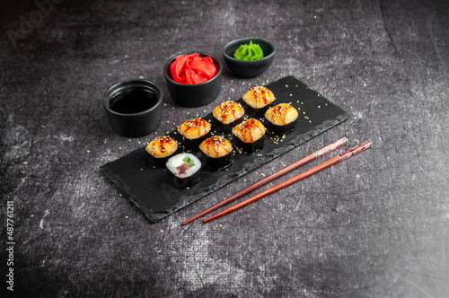 Assorted Japanese sushi on a black board with soy sauce, ginger, wasabi on a gray dark background