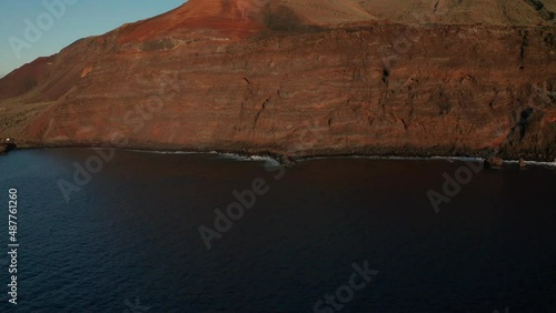 Aerial dolly over ocean to the red rock illuminated by the setting sun photo