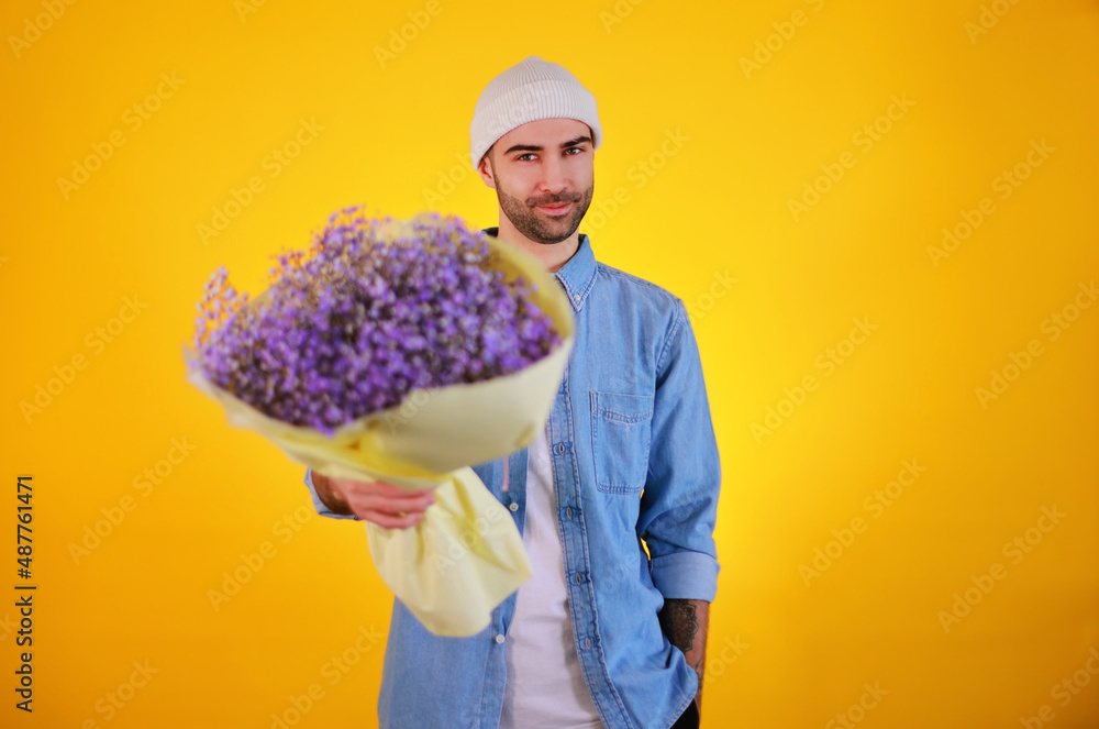 Handsome man with purple flowers. Women's day, 8 March selebration. Young male in jeans t-shirt on yellow background. Handsome man with purple flowers. Women's day, 8 March selebration. Young male in jeans t-shirt on yellow background.