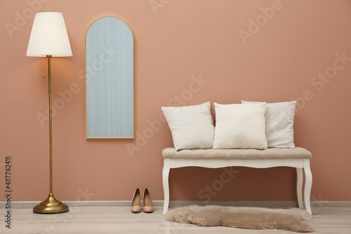 Room interior with white bench and mirror hanging on light pink wall. Stylish accessories