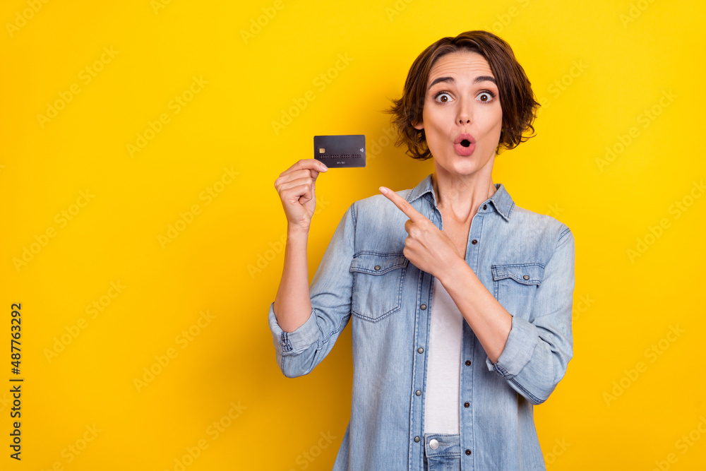 Photo of young impressed girl point finger bank card advertise select income isolated over yellow color background Photo of young impressed girl point finger bank card advertise select income isolated over yellow color background