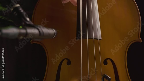 Male hands playing standup bass while recording with a microphone in foreground