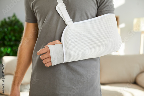 Close up of sling on broken arm of man he needs to wear during rehabilitation period. Unknown male patient wearing immobilizer after car accident or after sports injury. Orthopedics concept. photo