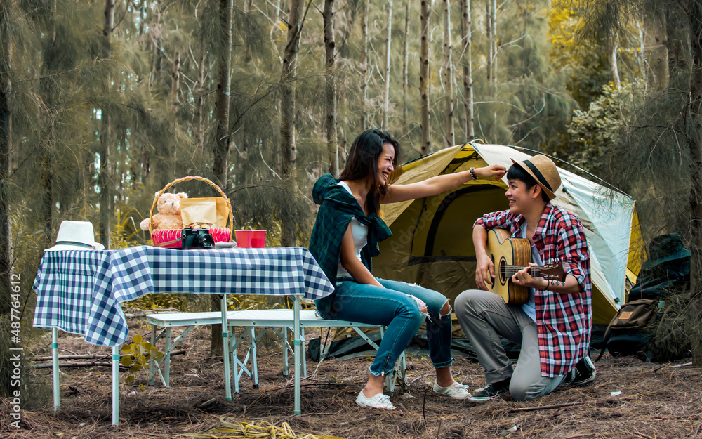 Asian sweet couple man and woman setting tent and camp in forest, playing guitar, adventure backpack traveling together with happiness and fun in vacation trip on weedkend. Lifestyle concept. Asian sweet couple man and woman setting tent and camp in forest, playing guitar, adventure backpack traveling together with happiness and fun in vacation trip on weedkend. Lifestyle concept.