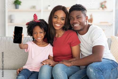 Cheerful african american family of three showing blank smartphone with black screen