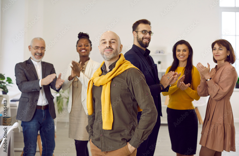 Portrait of happy proud middle-aged male employee forefront feel motivated, smiling diverse colleagues applaud on background. Multiethnic employees congratulate coworker with work promotion. Portrait of happy proud middle-aged male employee forefront feel motivated, smiling diverse colleagues applaud on background. Multiethnic employees congratulate coworker with work promotion.