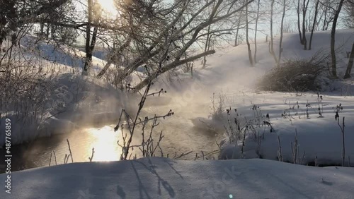 frost and sun, a wonderful day. view of the vapors over the river on a winter morning with the sun shining through the branches in the village.