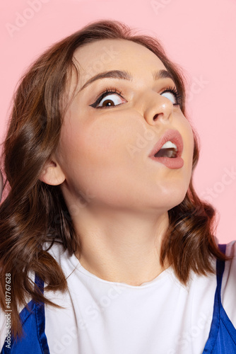 Close-up face of cute young girl crushed on glass isolated on light pink studio background. Concept of human emotions, facial expression, youth