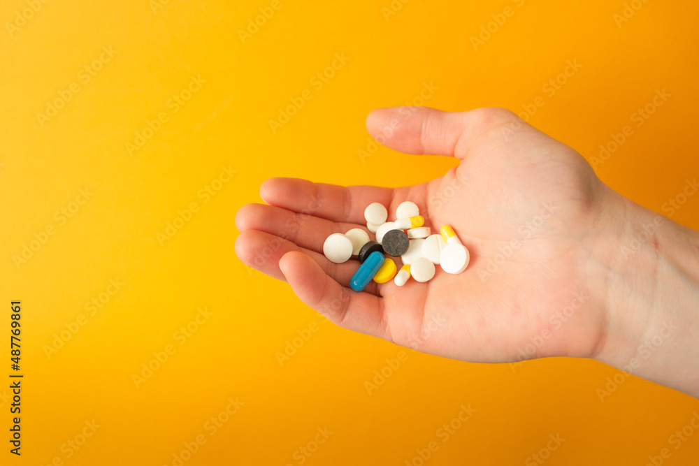 Man's palm holds a handful of different multicolored pills, capsules and drops. Yellow background. Health care concept.