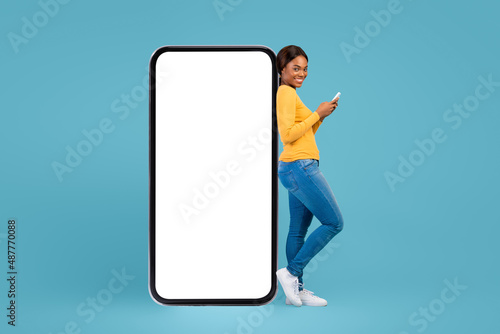 Cheerful Black Woman Holding Cellphone And Leaning At Big Blank Mobile Phone © Prostock-studio