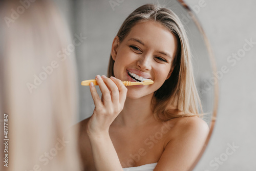 Oral hygiene, healthy teeth and care. Young woman brushing teeth with toothbrush and looking in mirror in bathroom photo