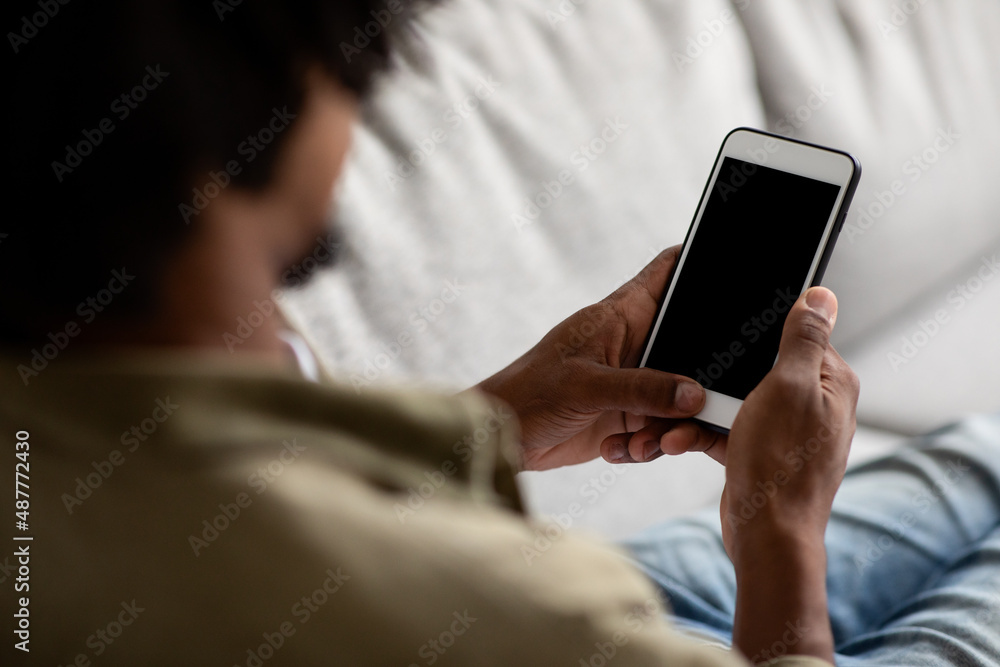 Over Shoulder Shot Of Black Male Using Blank Smartphone At Home Over Shoulder Shot Of Black Male Using Blank Smartphone At Home