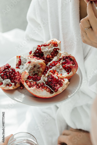 A girl in a white coat tastes a juicy red pomegranate