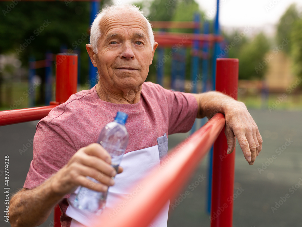 Fototapeta premium Mature man quenches her thirst from bottle after jogging in park