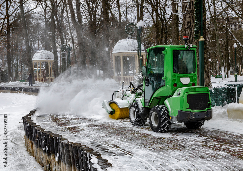 Snowplow on snow removal in the park puffs of snow from under a working machine Snowplow on snow removal in the park puffs of snow from under a working machine