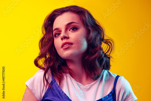 Close-up pretty girl with long curly hair in retro style attire isolated on orange background in neon light, filter. Concept of emotions, beauty, fashion