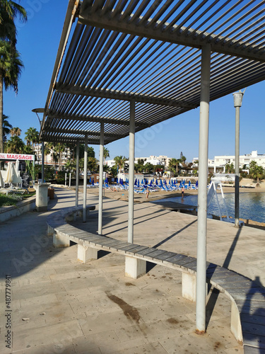 Protaras. Famagusta area. Cyprus. Promenade with a bench and a sunshade, going along the Mediterranean coast to the beach.