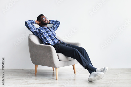 Peaceful young black man relaxing in armchair against white studio wall, free space © Prostock-studio