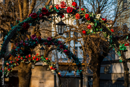 Alley under an iron arch decorated with red roses with a lantern. Spring city beautiful landscape. Red roses on the arch. High quality photo © Silviya Stoyanova