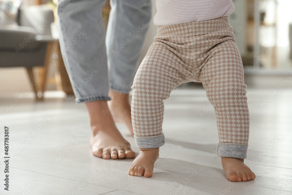 Mother supporting her baby daughter while she learning to walk at home, closeup