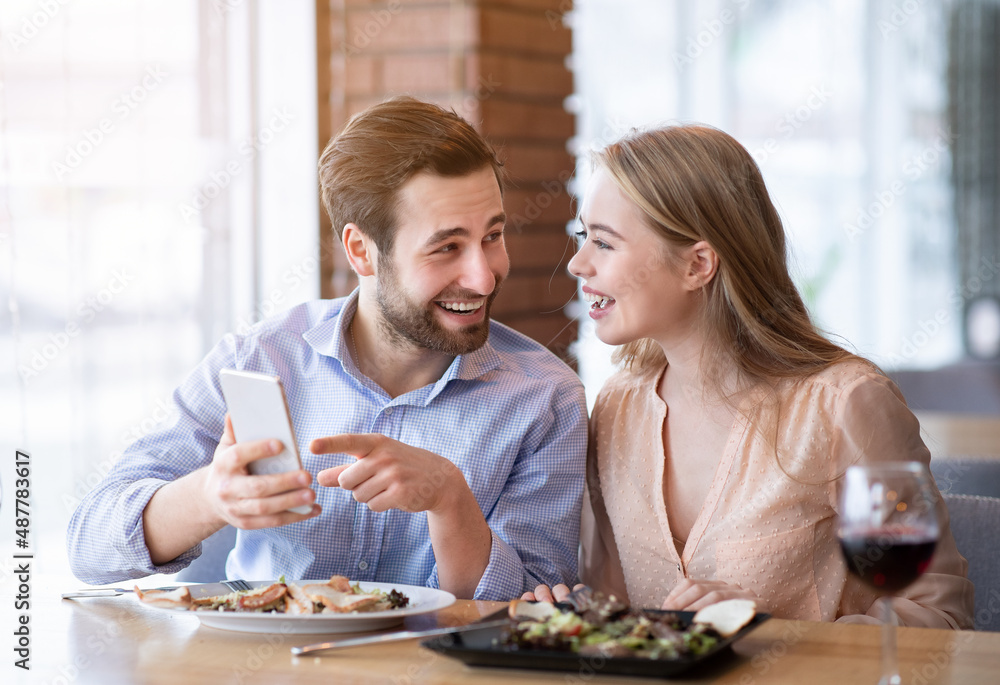 Happy young spouses checking their smartphone during romantic dinner at restaurant