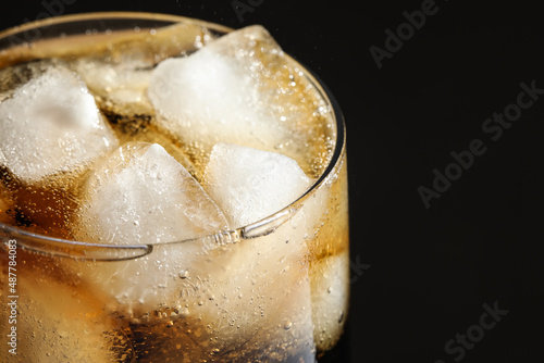 Glass of refreshing soda drink with ice cubes on black background, closeup