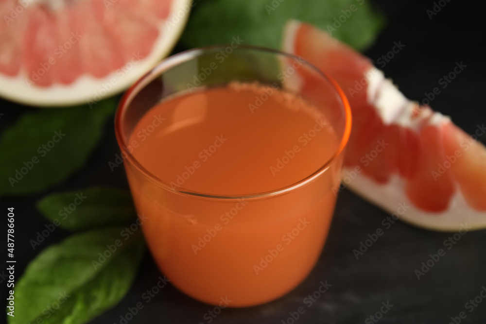 Glass of pink pomelo juice and green leaves on black table, closeup Glass of pink pomelo juice and green leaves on black table, closeup
