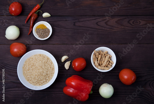 Products rice, vegetables, spices and soy meat for cooking jollof rice on a brown wooden background. National cuisine of Africa. Copy spaes.