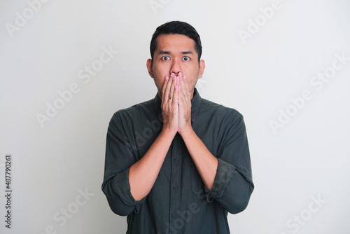 Adult Asian man showing shocked expression with his hands covering mouth photo