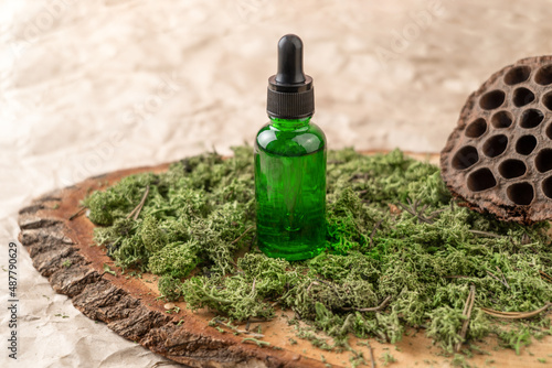 A green dropper bottle of face serum or natural oil standing on a moss