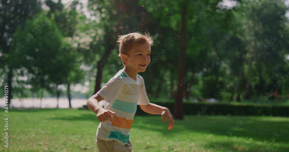 Happy boy running in green park. Joyful kid playing catch-up on weekend outdoors Happy boy running in green park. Joyful kid playing catch-up on weekend outdoors