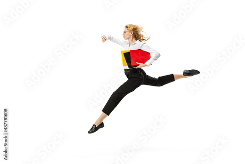 Dynamic portrait of young pretty girl wearing business style clothes jumping with folders isolated on white background. Finance, ballet, art, business, beauty concept.