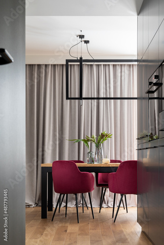 Stylish composition of kitchen and dining room open space interior. Minimalist ergonomic kitchen space. Velvet chairs, wooden table and personal accessories in the modern dining room. Template.