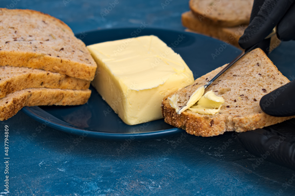 chef in gloves spreads butter with a knife on a slice of bread.