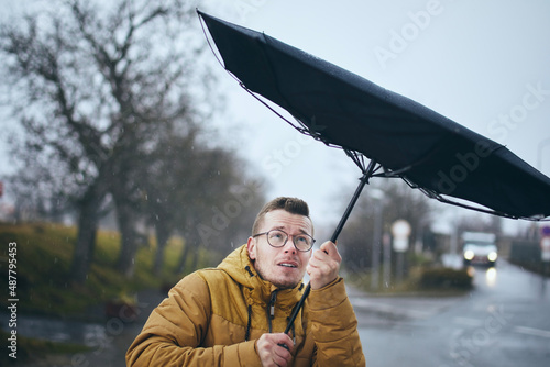 Canvas Print Man holding broken umbrella in strong wind during gloomy rainy day