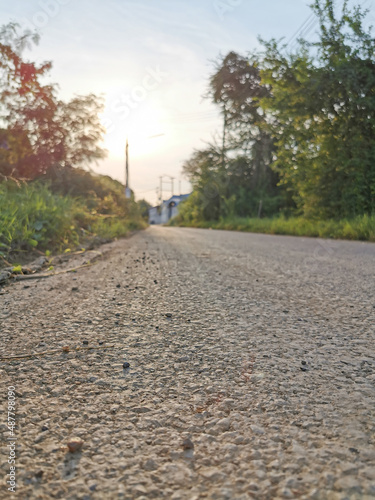 A rough concrete road with small and large gravel heading straight ahead in the evening 