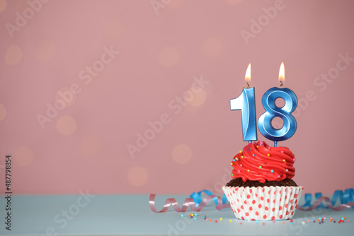 Coming of age party - 18th birthday. Delicious cupcake with number shaped candles on light blue table, space for text photo