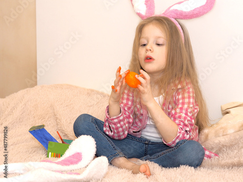 A little blonde girl with bunny ears paints an Easter egg with a paintbrush. Easter preparation. Making Easter decor.
