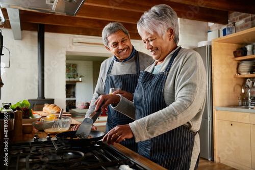 Elderly multi-ethnic couple laughing together in the kitchen. Happily retired and cooking breakfast with each other.